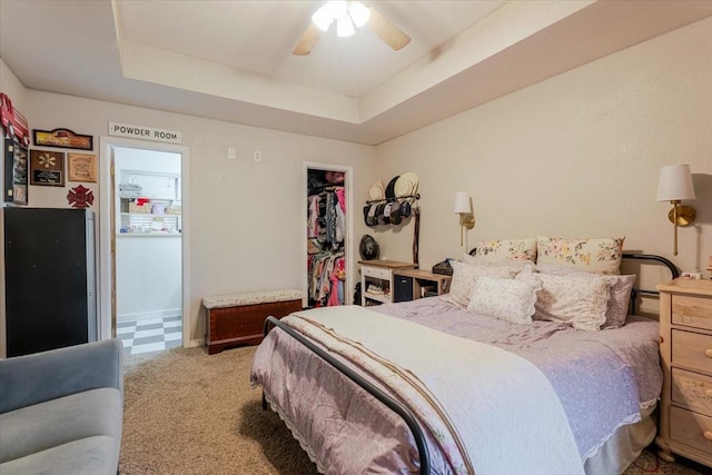 carpeted bedroom featuring a spacious closet, a closet, a raised ceiling, and a ceiling fan