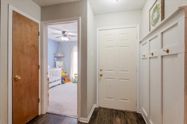 doorway with dark wood-type flooring, a textured wall, and baseboards