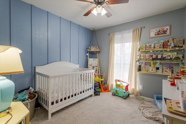 carpeted bedroom featuring a ceiling fan and a crib