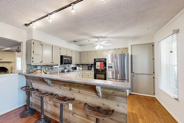 kitchen with light wood-style floors, a peninsula, light countertops, crown molding, and black appliances