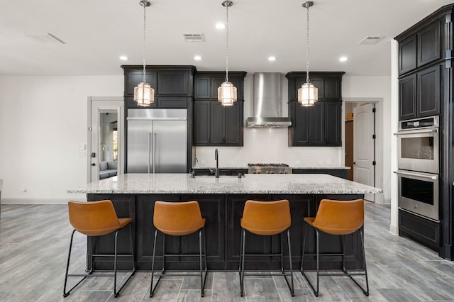 kitchen featuring visible vents, a spacious island, stainless steel appliances, wall chimney range hood, and a sink