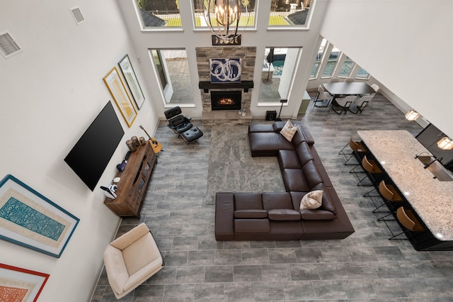 living area featuring a stone fireplace, a high ceiling, visible vents, and an inviting chandelier