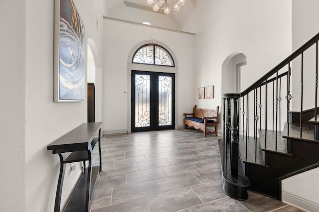 entrance foyer with arched walkways, french doors, a notable chandelier, stairway, and a high ceiling