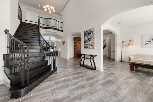 foyer entrance featuring stairs, a chandelier, arched walkways, and baseboards