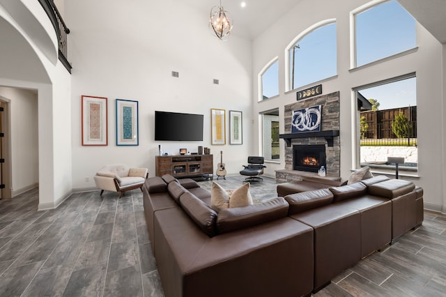 living area with a notable chandelier, visible vents, wood tiled floor, a stone fireplace, and baseboards