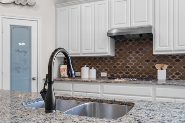 kitchen with tasteful backsplash, a sink, white cabinetry, and under cabinet range hood