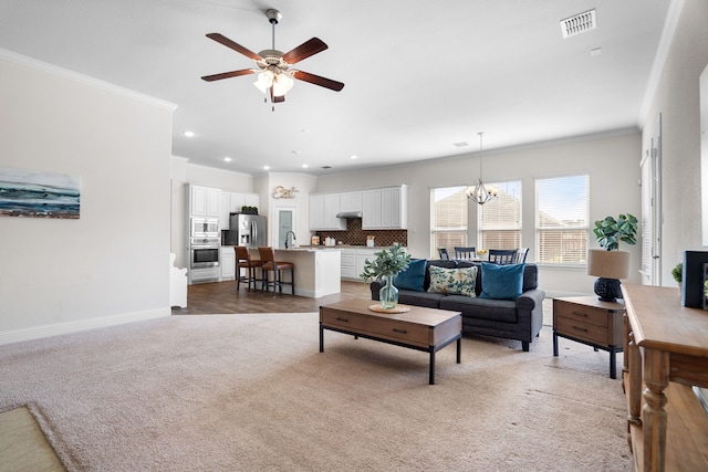 living room with visible vents, baseboards, light colored carpet, crown molding, and ceiling fan with notable chandelier