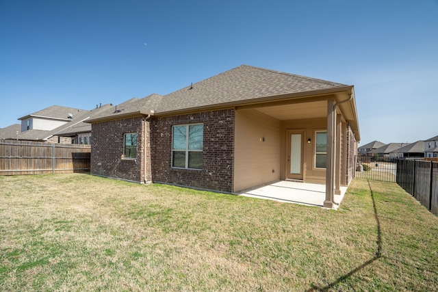 back of property with a fenced backyard, brick siding, a yard, roof with shingles, and a patio area