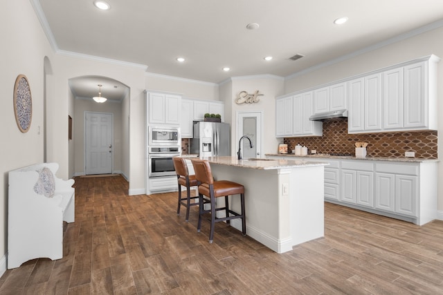 kitchen with arched walkways, under cabinet range hood, stainless steel appliances, a sink, and visible vents