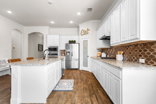 kitchen featuring under cabinet range hood, stainless steel appliances, visible vents, backsplash, and dark wood-style floors