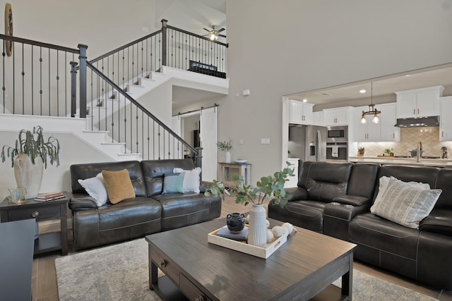 living area featuring a barn door, stairway, light wood-style flooring, and a ceiling fan