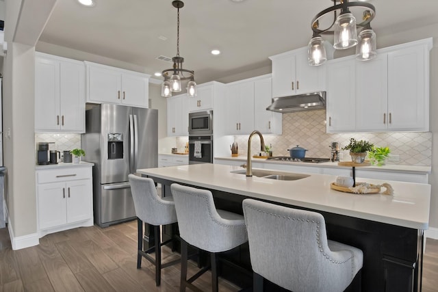 kitchen with appliances with stainless steel finishes, wood finished floors, light countertops, under cabinet range hood, and a sink