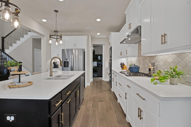 kitchen with visible vents, stainless steel appliances, dark cabinetry, under cabinet range hood, and a sink