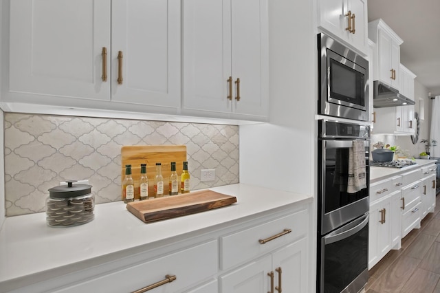 kitchen featuring tasteful backsplash, light countertops, appliances with stainless steel finishes, white cabinetry, and under cabinet range hood