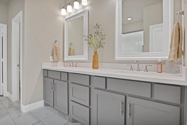 full bath with marble finish floor, double vanity, a sink, and baseboards