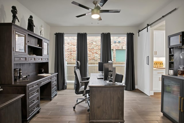 office area featuring a ceiling fan, wood tiled floor, visible vents, and a barn door