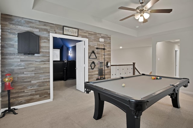 recreation room featuring wooden walls, an accent wall, a raised ceiling, and light colored carpet