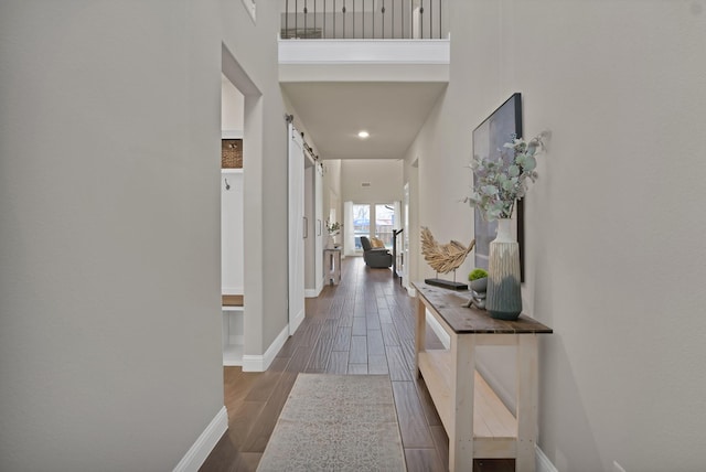 hallway with a barn door, wood tiled floor, and baseboards