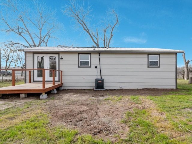 back of property featuring metal roof, a lawn, a wooden deck, and central AC unit