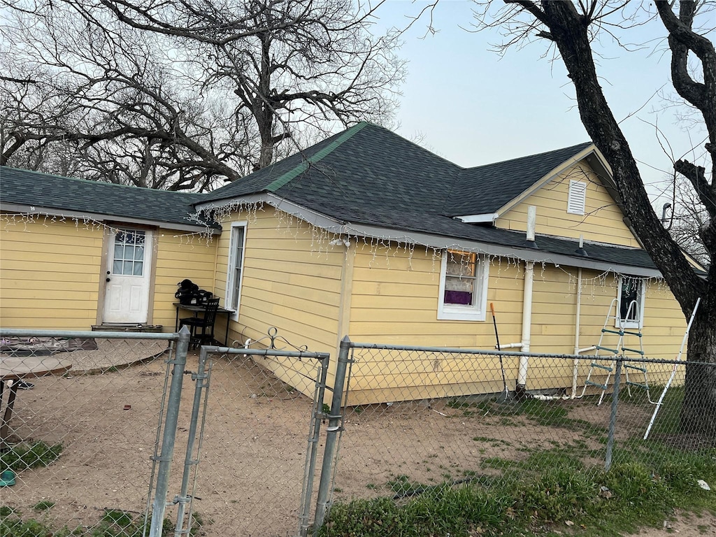 view of side of property with a shingled roof, a gate, and fence