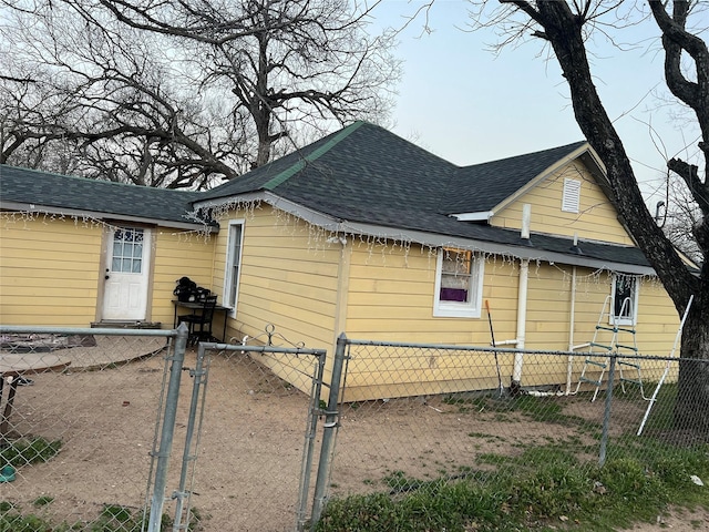 view of side of property with a shingled roof, a gate, and fence