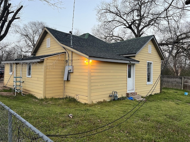 back of house with entry steps, a yard, roof with shingles, and fence