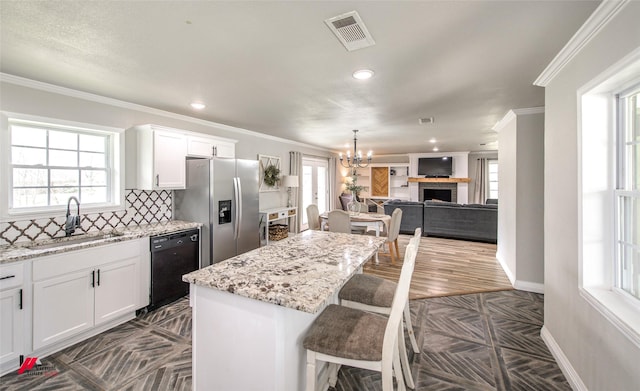 kitchen featuring a sink, visible vents, a kitchen breakfast bar, dishwasher, and stainless steel fridge