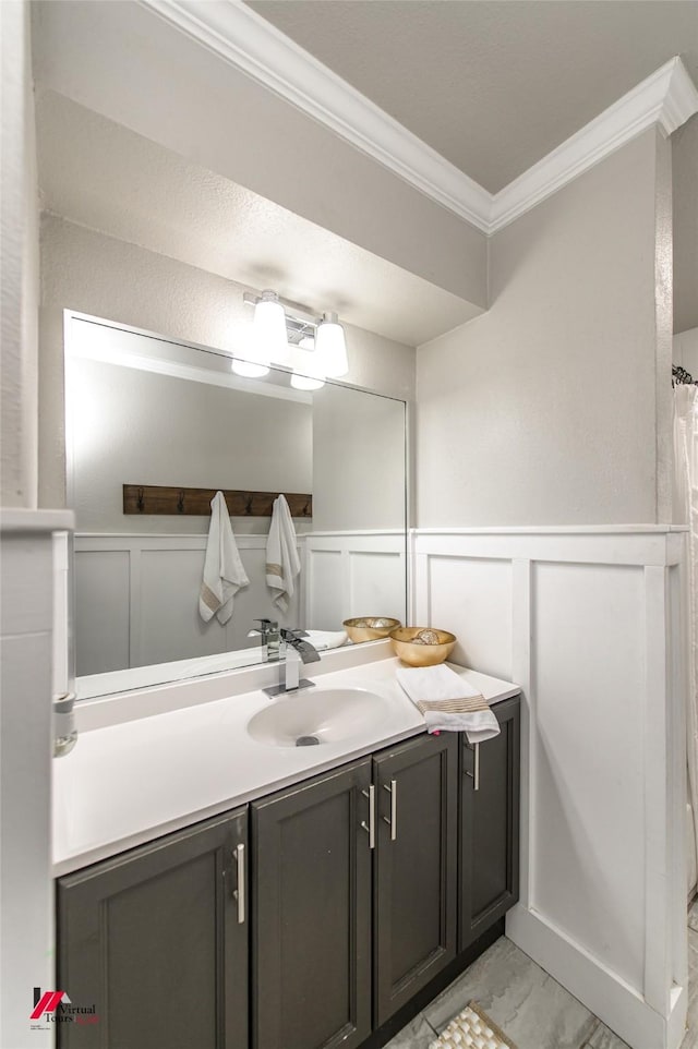 full bathroom with a decorative wall, vanity, marble finish floor, wainscoting, and crown molding