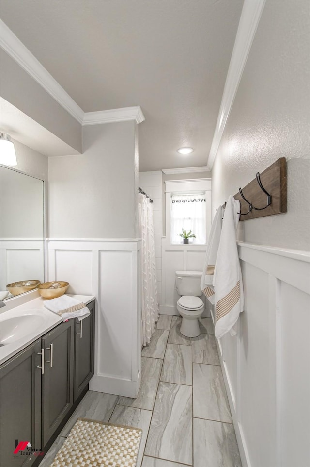 bathroom with toilet, a decorative wall, a wainscoted wall, vanity, and ornamental molding