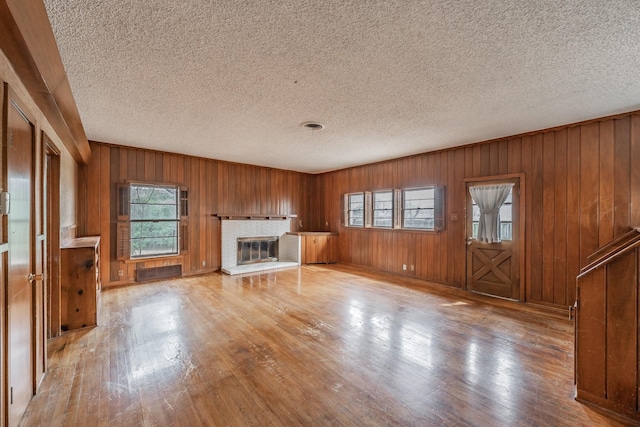 unfurnished living room with a brick fireplace, wood-type flooring, visible vents, and a textured ceiling