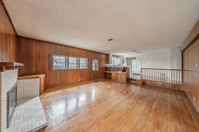 unfurnished living room featuring light wood-style floors, a brick fireplace, wood walls, and a textured ceiling