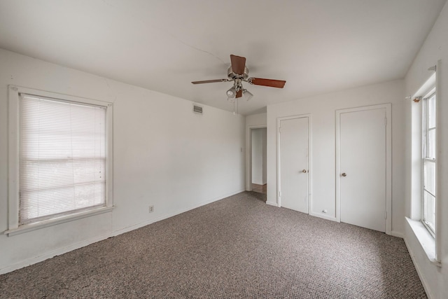 unfurnished bedroom featuring carpet, visible vents, ceiling fan, and two closets