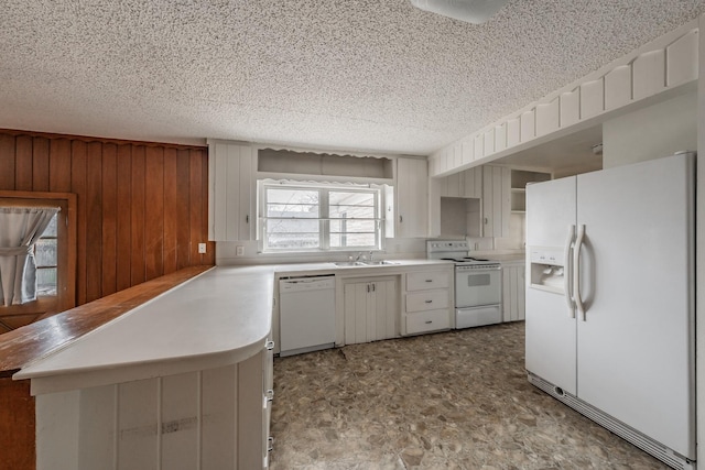 kitchen with white appliances, wooden walls, a peninsula, light countertops, and a sink