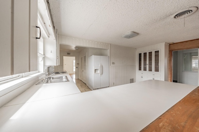 kitchen featuring white fridge with ice dispenser, visible vents, a sink, and a peninsula