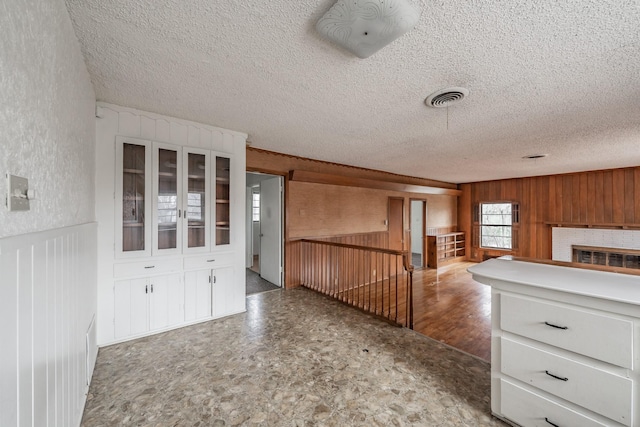 kitchen with visible vents, a brick fireplace, white cabinets, wood walls, and a textured ceiling