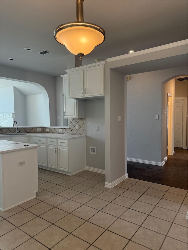 kitchen featuring tasteful backsplash, arched walkways, white cabinets, and light countertops