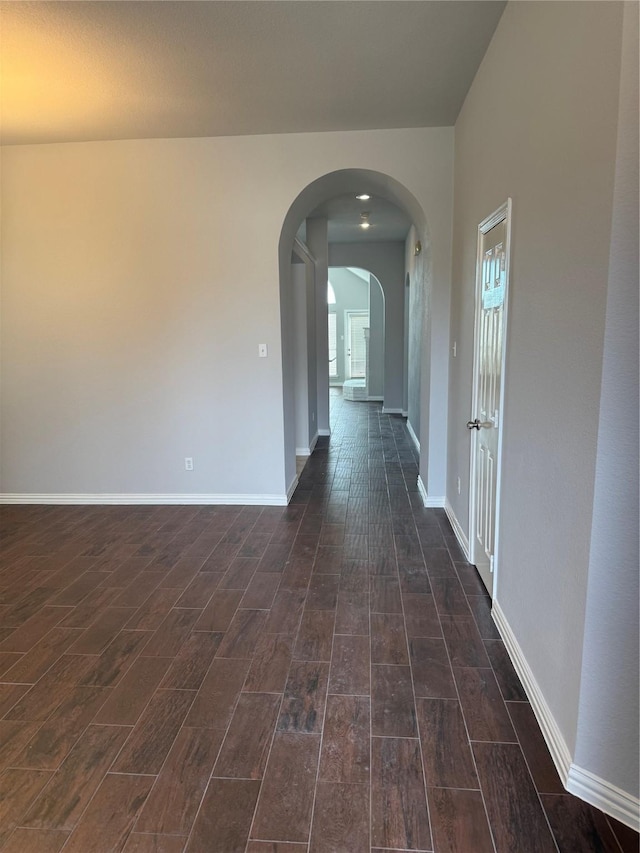 corridor with wood finish floors, arched walkways, and baseboards