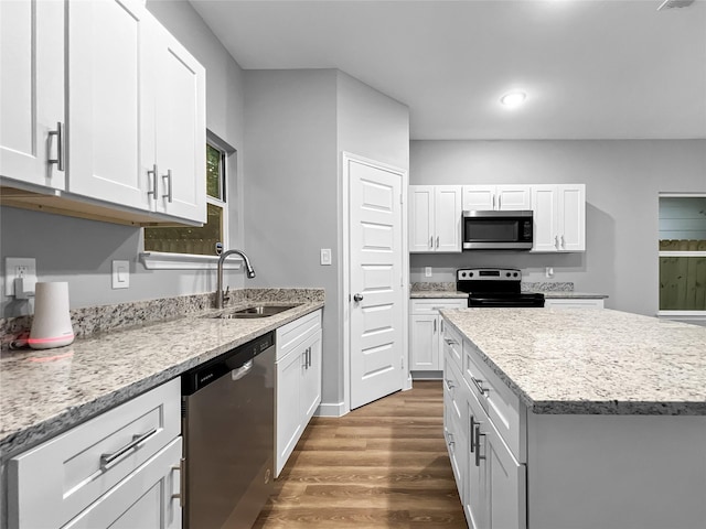 kitchen with white cabinets, light stone countertops, wood finished floors, appliances with stainless steel finishes, and a sink