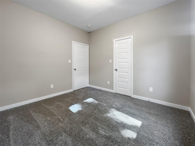 empty room featuring baseboards and dark colored carpet