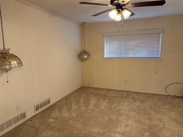 carpeted empty room with a ceiling fan, visible vents, and crown molding