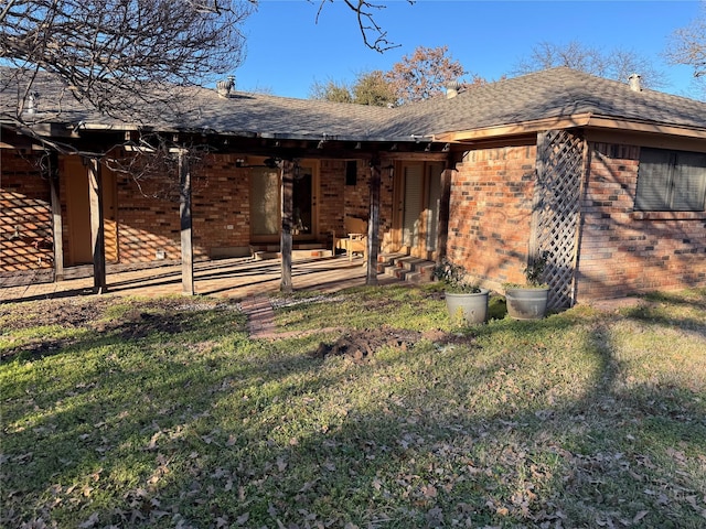 view of front of property with roof with shingles, brick siding, a front lawn, and a patio area