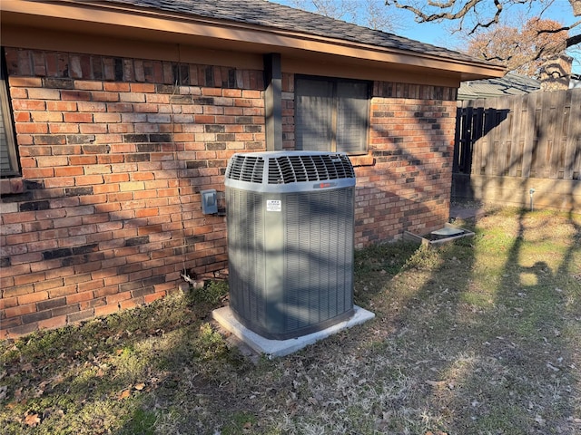 exterior details with roof with shingles, brick siding, fence, and central air condition unit