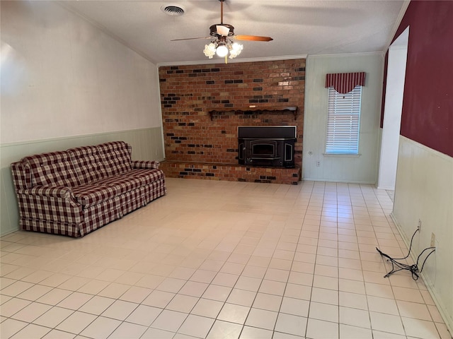 living area featuring light tile patterned floors, ceiling fan, visible vents, wainscoting, and crown molding