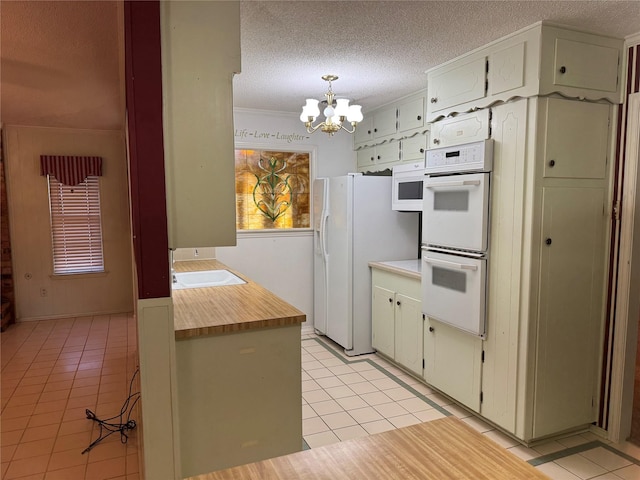 kitchen with light tile patterned flooring, a sink, a textured ceiling, a chandelier, and white appliances