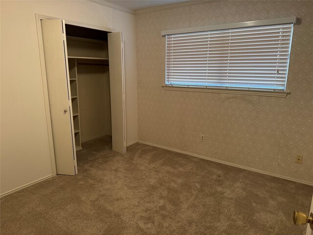 unfurnished bedroom featuring wallpapered walls, carpet, ornamental molding, and a closet