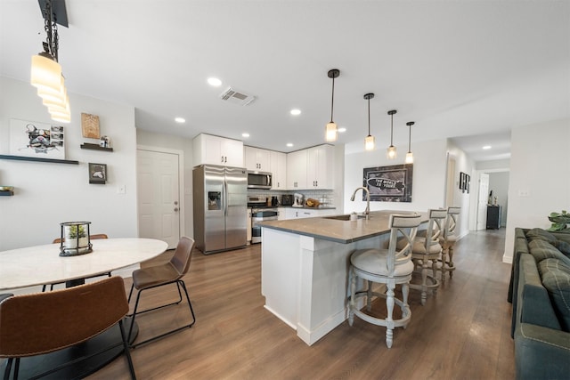 kitchen with appliances with stainless steel finishes, visible vents, a sink, and dark wood-type flooring