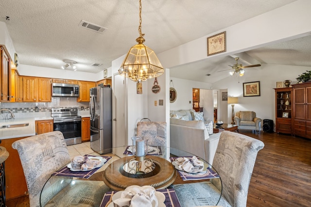 dining room with vaulted ceiling with beams, light wood finished floors, visible vents, a textured ceiling, and ceiling fan with notable chandelier