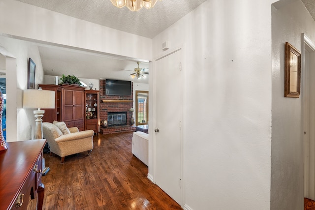 living area featuring dark wood-style floors, ceiling fan, a fireplace, and a textured ceiling