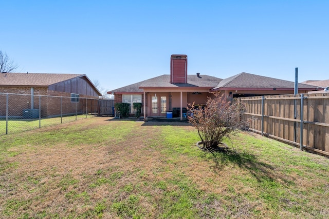 back of property with a fenced backyard, a yard, and a chimney