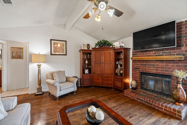 living room featuring visible vents, lofted ceiling with beams, wood finished floors, a textured ceiling, and a brick fireplace